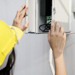 técnico usando capacete amarelo fazendo manutenção em uma caixa branca de energia